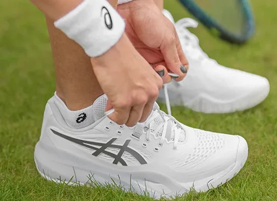 Person tying a white ASICS tennis shoe