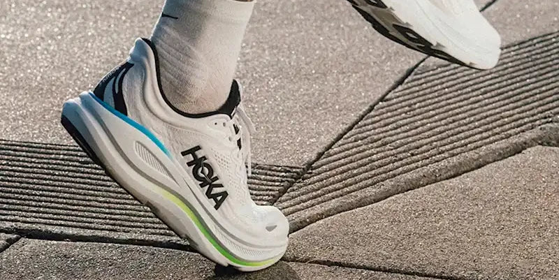 Runner wearing white HOKA shoes on a paved path