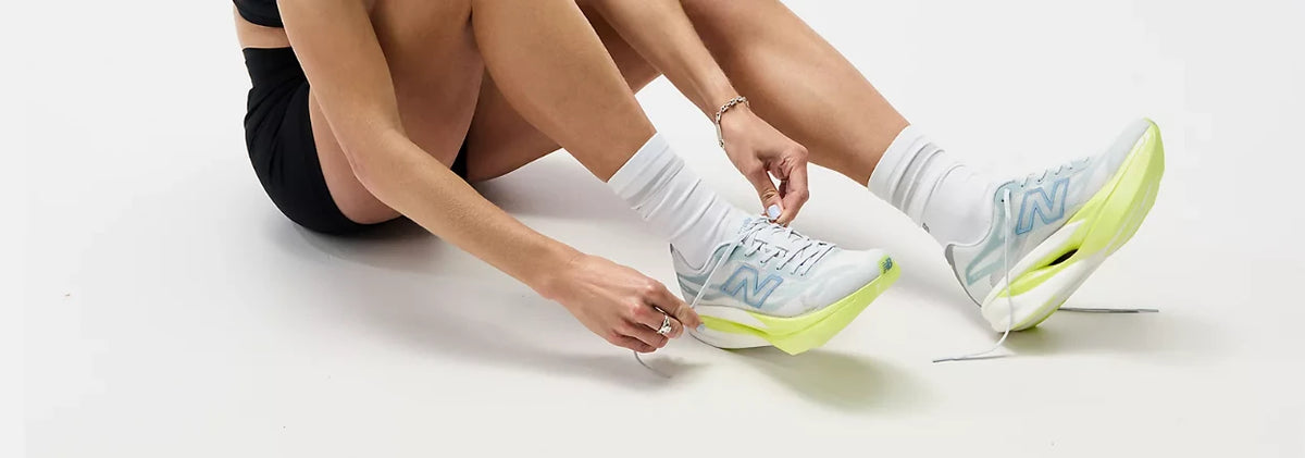 Person tying white and yellow New Balance running shoes